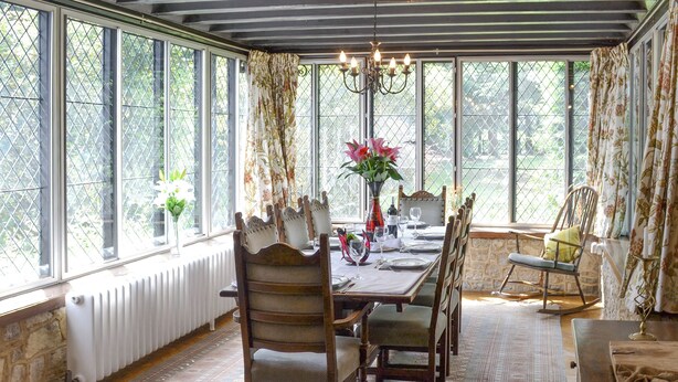 A dining area with a long table set for four, surrounded by chairs, a chandelier, and large windows with curtains. - 3 bedroom accommodation in Little Chart, near Ashford (Little Chart, near Ashford)