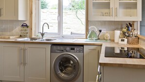 Une cuisine compacte équipée d’un lave-linge, d’un évier et d’une fenêtre donnant sur un espace verdoyant.