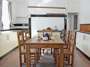A kitchen with a wooden table and chairs, a kettle, a jug, and a bowl.