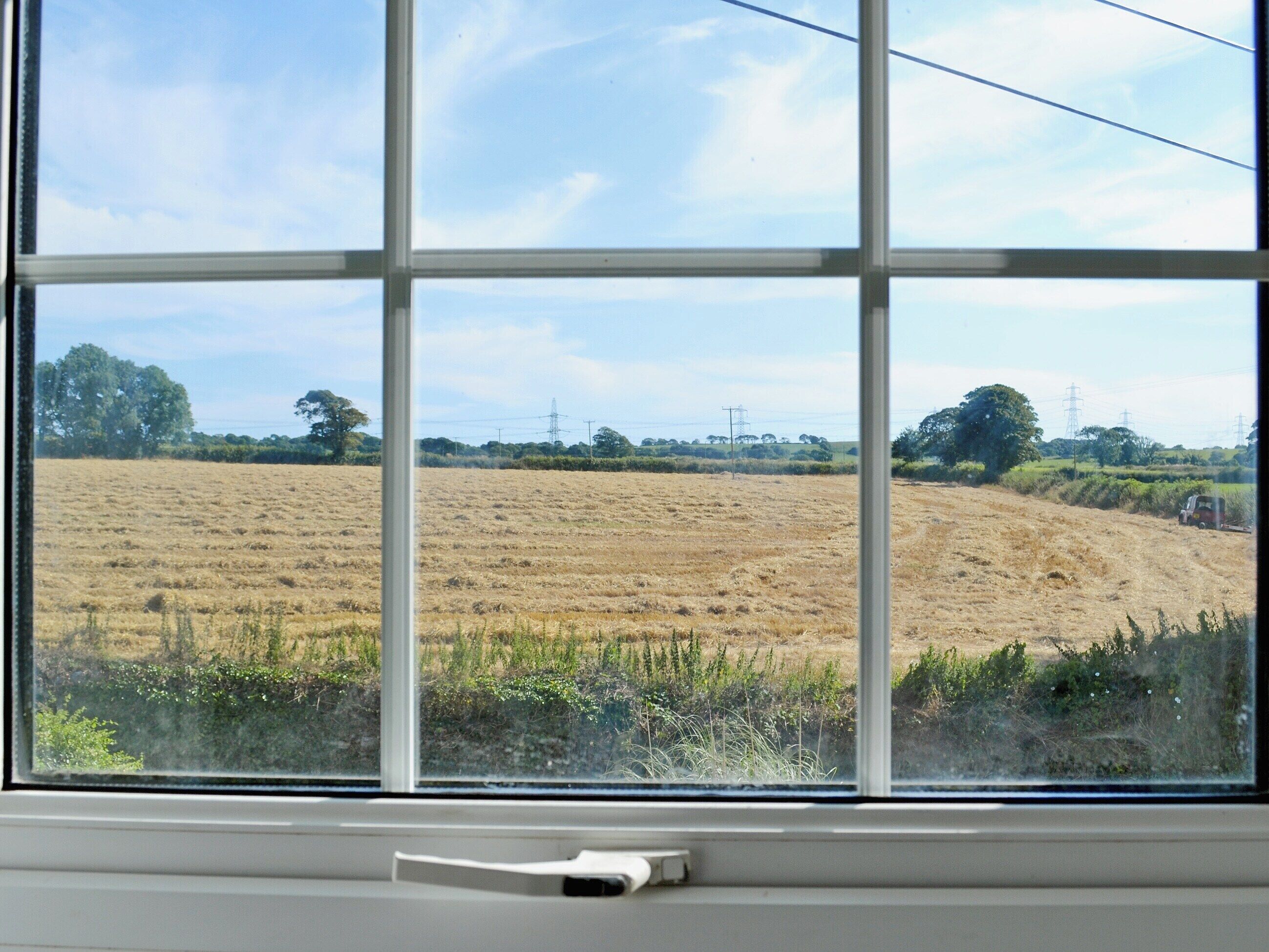 Blick durch ein Fenster auf ein Feld mit Stromleitungen in der Ferne.