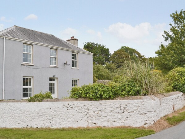 A two-story house with a stone wall in front, surrounded by greenery.