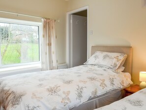 Een slaapkamer met een bed, nachtkastje, raam met gordijnen en een deur.