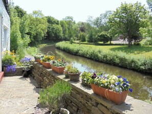A stone pathway leading to a canal with potted flowers and lush greenery.
