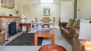 Ein Wohnzimmer mit Kamin, einem braunen Ledersofa, einem Holztisch und einem Essbereich mit Korbstühlen.