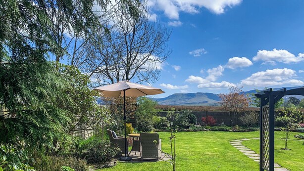 Ein gepflegter Garten mit einer Terrassenfläche, einem gepflasterten Weg und einer Pergola.