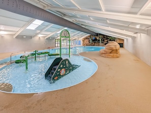Une piscine intérieure dotée d’un toboggan, d’une structure rocheuse et d’une arche verdoyante.