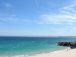 Une plage avec un ciel dégagé, une eau calme et une terre visible au loin.