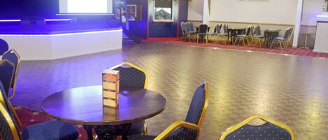 A conference room with a round table, blue chairs, a projector screen, and a stage area.