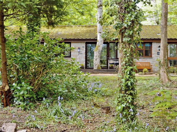 Un bâtiment rustique aux murs de pierre, doté d’un toit en tuiles et d’un banc en bois dans la cour.