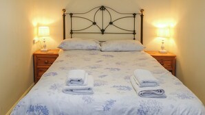 Un lit bien fait, avec une literie à motifs floraux, deux lampes de chevet et des serviettes pliées posées sur le lit.