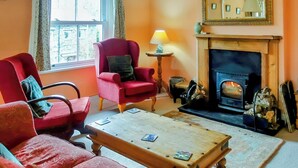 Un salon chaleureux avec des meubles rembourrés de couleur rouge, une table basse en bois, une cheminée et une fenêtre avec des rideaux.