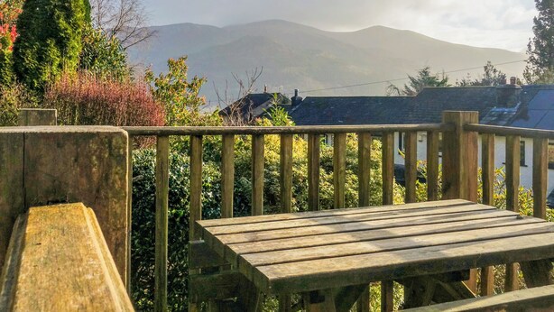 Une terrasse en bois avec un banc, entourée de verdure et offrant une vue sur une chaîne de montagnes.