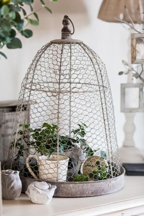 Une cage à oiseaux en fil de fer contenant des plantes et des pots de fleurs, posée sur une étagère.