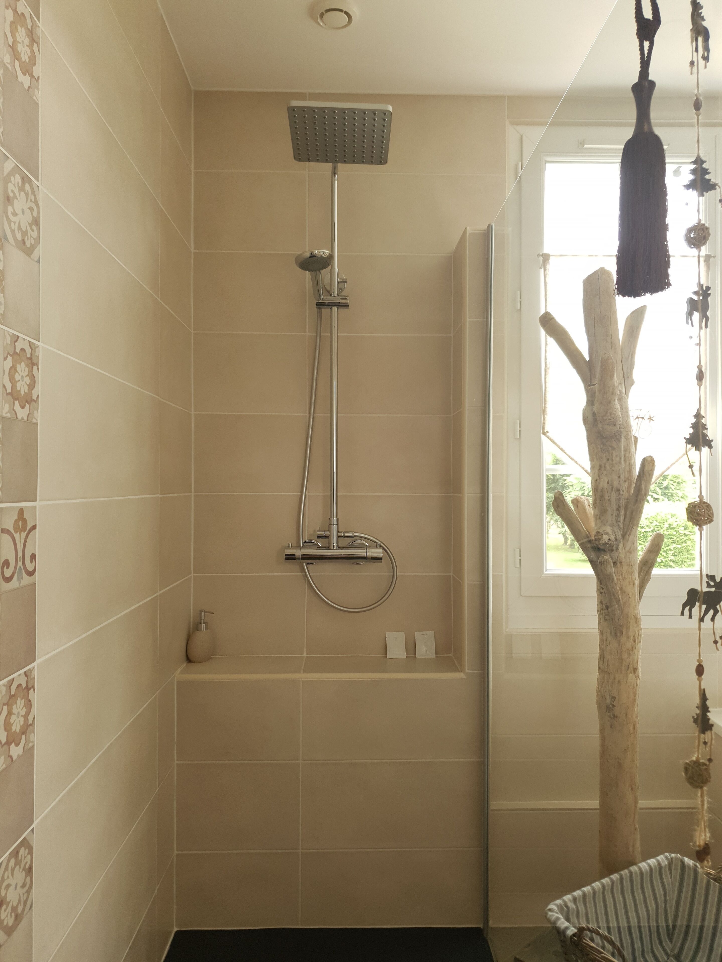 A shower with a handheld showerhead and a wall-mounted panel, a small bathtub, and a window with a view of greenery.