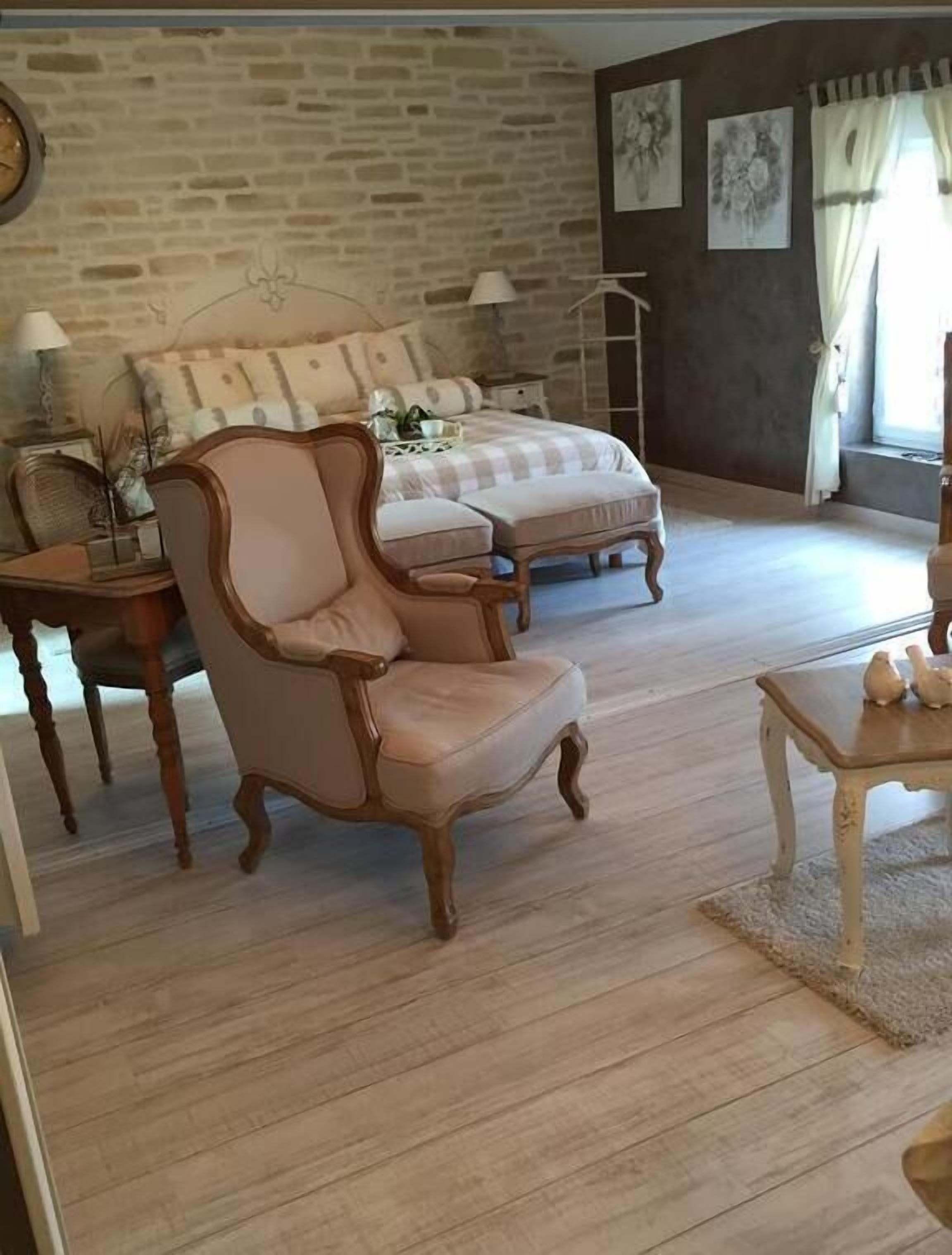 A bedroom with a bed, a chair, a nightstand, and a lamp.