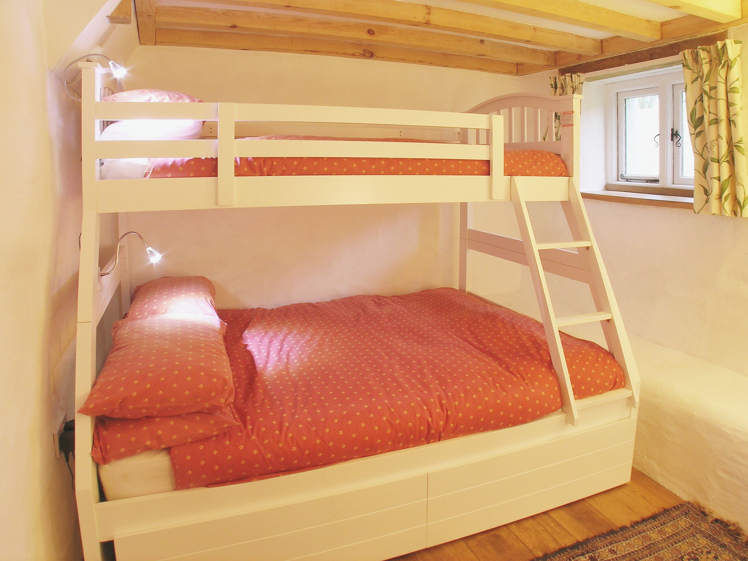 A bunk bed with a ladder, a bedside table, and a window with curtains.