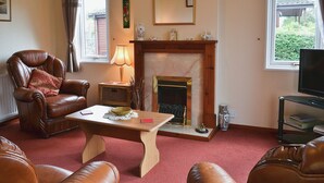 A living room with a fireplace, leather furniture, a table, and a television.