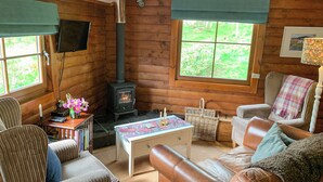 Un interior de cabaña acogedor con detalles de madera, una chimenea, un televisor montado en la pared y un área de estar cómoda con un sofá y sillones.