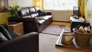 A living room with a brown leather sofa, a small wooden table, a television on a stand, and a window with blinds. - 2 bedroom accommodation in Brampton, nr Appleby (Brampton, nr Appleby)