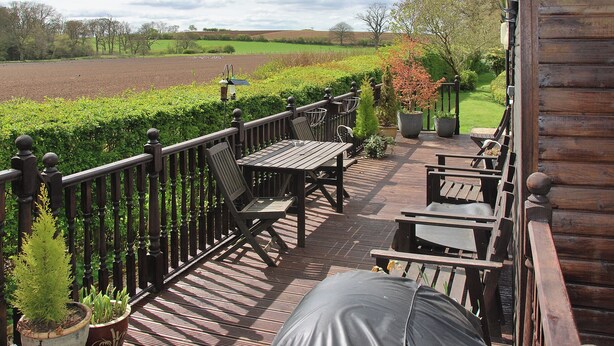 A wooden deck with outdoor furniture, a view of a field, and a hedge. - 2 bedroom accommodation in Brampton, nr Appleby (Brampton, nr Appleby)