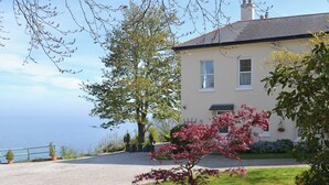 Ein Haus mit Kiesweg, einem großen Baum davor und Blick aufs Meer.