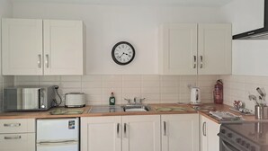 Eine Küche mit weißen Schränken, einem Kühlschrank, einem Toaster, einer Spüle, einer Uhr und einem Herd.