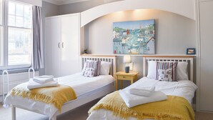 Un dormitorio con dos camas individuales, una mesita de noche, una lámpara, un cuadro y una ventana con cortinas.