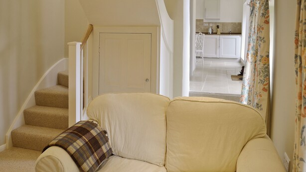 A staircase leading to a door, a sofa with a plaid throw, and a view into a kitchen area. - 1 bedroom accommodation in Laverton, near Ripon (Laverton, near Ripon)