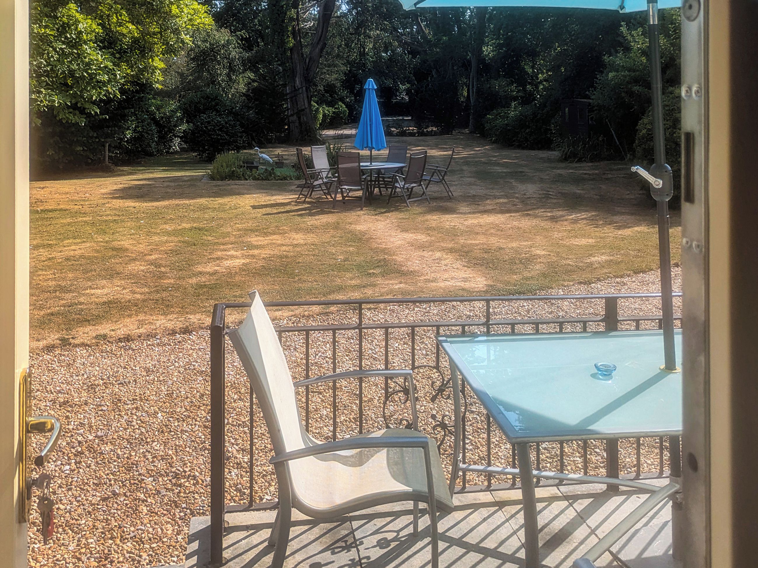 A patio with a table and chairs, a blue umbrella, and a pebbled ground.
