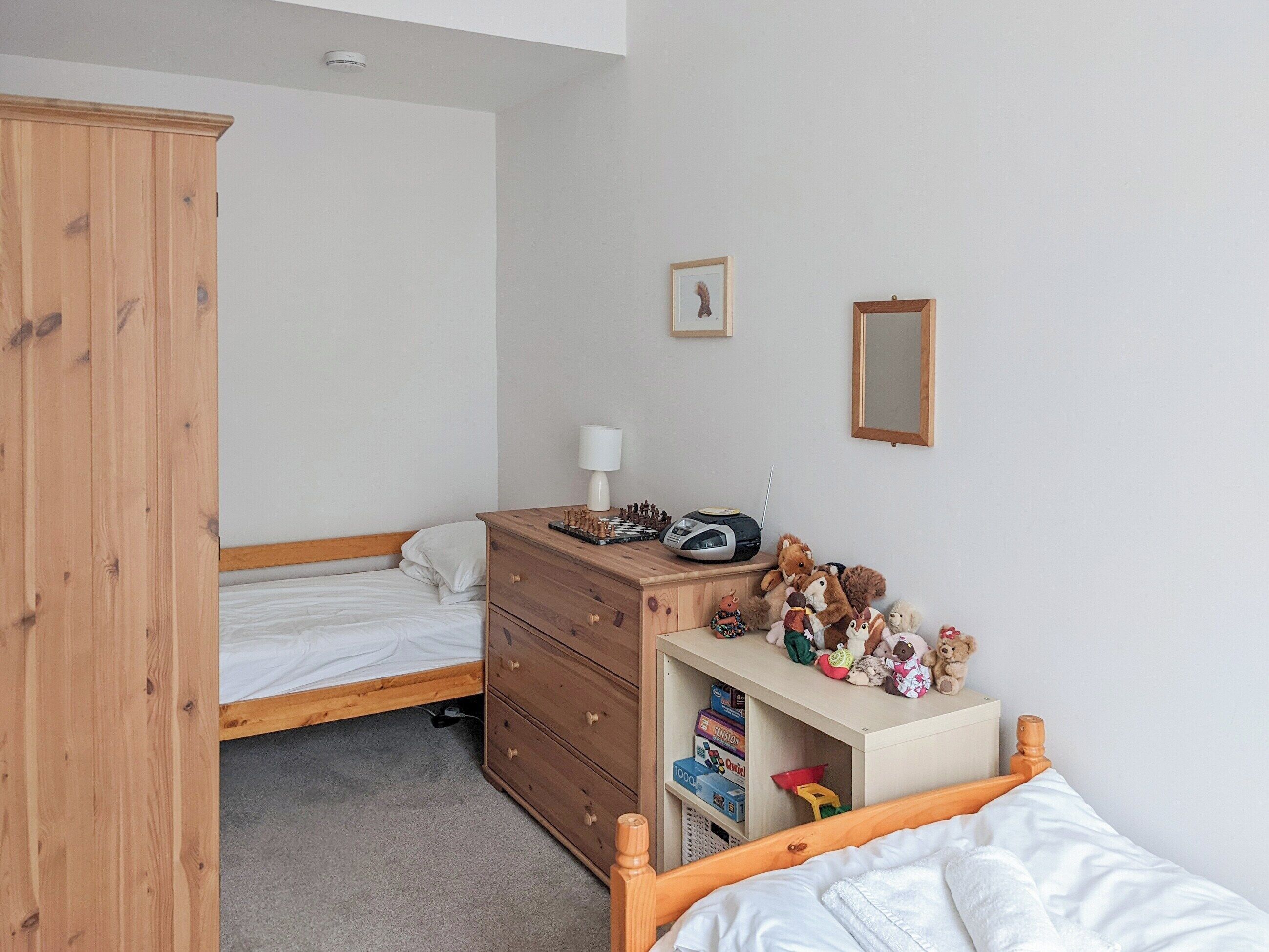 Un dormitorio con un armario de madera, una cama con ropa de cama blanca, un aparador con juguetes y una radio.