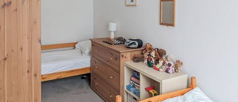 Un dormitorio con un armario de madera, una cama con ropa de cama blanca, un aparador con juguetes y una radio.