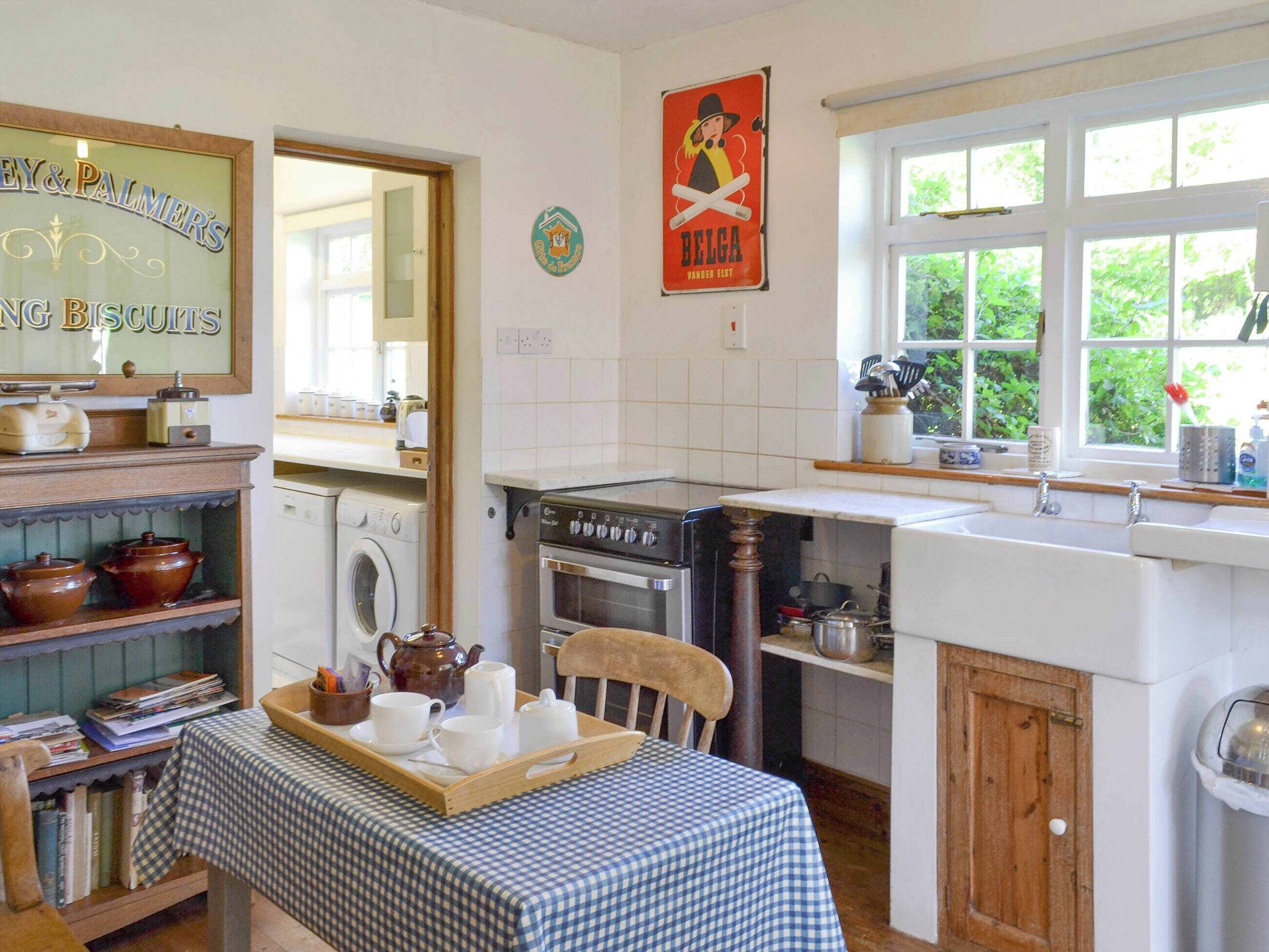 A kitchen with a washing machine, an oven, a sink, and a table with a tray of cups and a teapot.