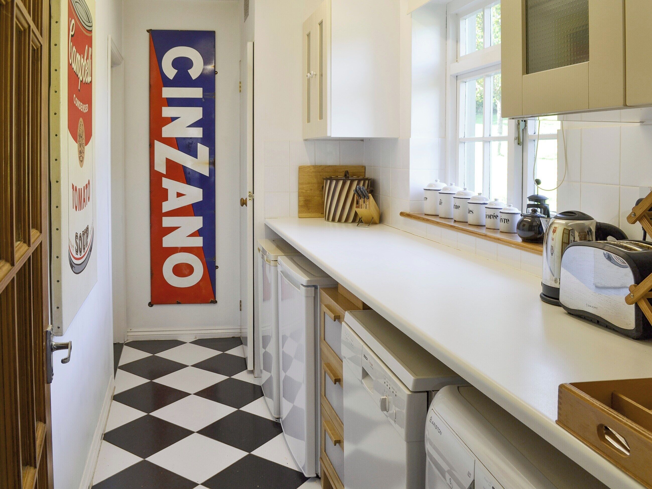 Une cuisine avec un carrelage à motifs, des placards blancs, un grille-pain et une grande enseigne « CINZANO » accrochée au mur.