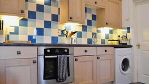 Une cuisine avec un dosseret à carreaux, des armoires en bois, un four en acier inoxydable, un lave-linge et un plan de travail sur lequel sont disposés divers objets.