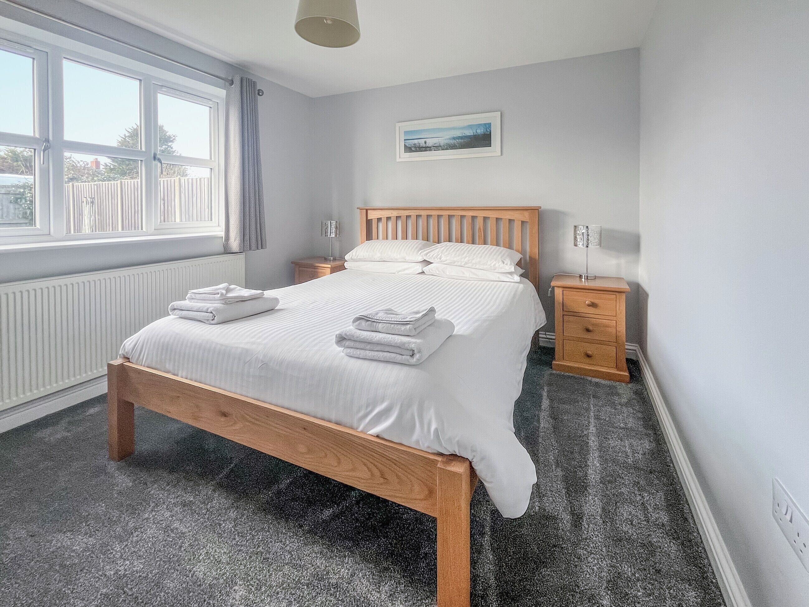 A neatly made bed with white linens and towels, a wooden headboard, a nightstand with a lamp, and a framed picture on the wall.