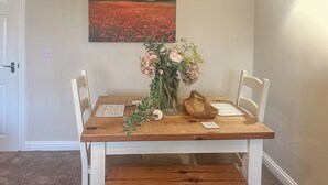 A wooden dining table with white chairs, a vase of flowers, and a wooden bowl. - 2 bedroom accommodation in Sutton-on-Sea, near Mablethorpe (Sutton-on-Sea, near Mablethorpe)