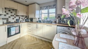 A modern kitchen with wooden cabinets, a tiled backsplash, a built-in oven, a dishwasher, and a window with a view of greenery. - 2 bedroom accommodation in Sutton-on-Sea, near Mablethorpe (Sutton-on-Sea, near Mablethorpe)