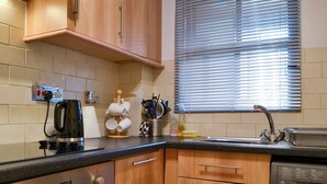 A modern kitchen with wooden cabinets, a built-in oven, a coffee maker, and a dishwasher. - Bleaberry- Hewetson Court (Keswick)