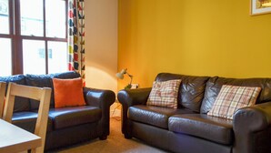 A living room with two dark leather sofas, a wooden table, and a lamp on a side table. - Bleaberry- Hewetson Court (Keswick)