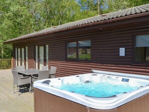 A wooden cabin with a hot tub on the deck, surrounded by a wooden deck and wicker furniture.