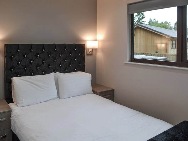 A bedroom with a tufted headboard, a bed with white linens, a bedside table, and a window with a view of a building.