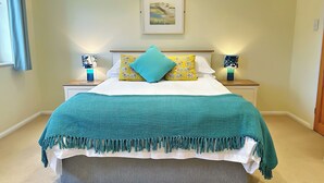 Quarto com cama, duas mesinhas de cabeceira, um criado-mudo, um quadro na parede e uma janela com cortinas.