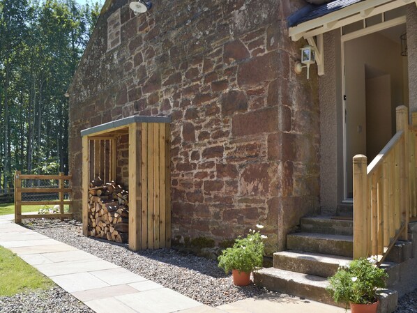 A stone building with a wooden entrance, steps, a wooden fence, and a gravel path.