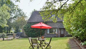 Une terrasse avec une table et des chaises, un parasol rouge et, au fond, une maison en briques.