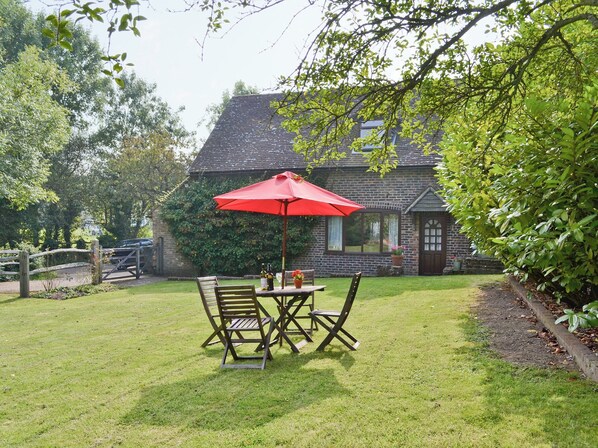 Une terrasse avec une table et des chaises, un parasol rouge et, au fond, une maison en briques.