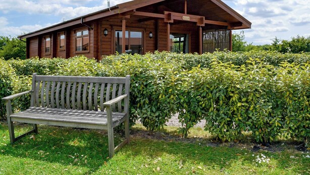 A wooden cabin with a sloped roof, large windows, and a bench in front. - 3 bedroom accommodation in Burgh le Marsh, near Skegness (Burgh le Marsh, near Skegness)