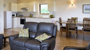 A modern kitchen with white cabinets, a microwave, and a kettle. There is a dining area with wooden chairs and a table. - 3 bedroom accommodation in Burgh le Marsh, near Skegness (Burgh le Marsh, near Skegness)