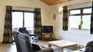 A living room with leather sofas, a wooden coffee table, a TV on a stand, and large windows with curtains. - 3 bedroom accommodation in Burgh le Marsh, near Skegness (Burgh le Marsh, near Skegness)
