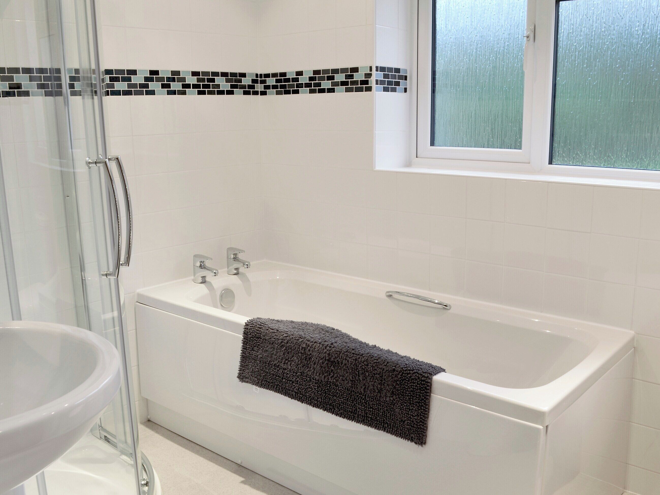 A bathroom with a bathtub, a glass shower enclosure, and a window.