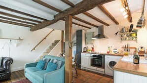 Un salon chaleureux avec un canapé bleu et un tapis à motifs rouges, une cuisine équipée d’appareils modernes et un escalier menant à l’étage.